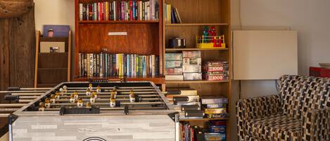 A room with a foosball table, a bookshelf, and a patterned armchair.