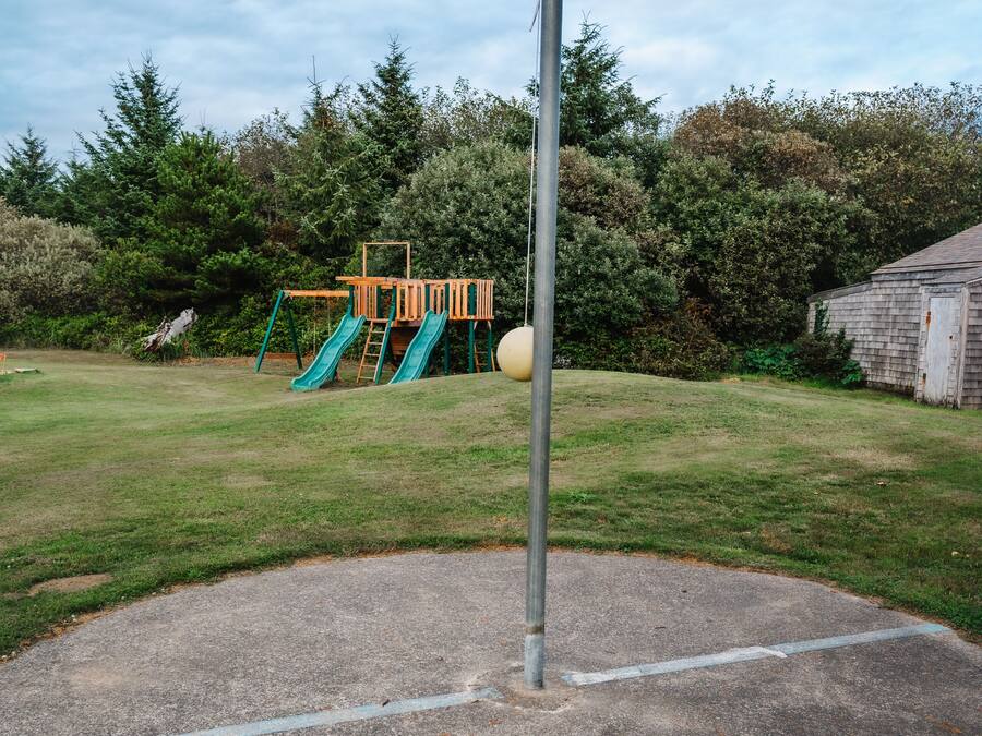 Een speeltuin met een glijbaan en schommels, omgeven door grasvelden en bomen.
