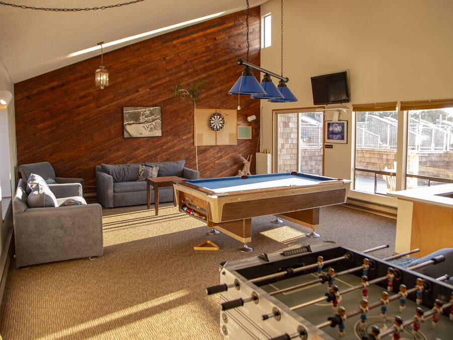 A cozy living room with a pool table, sofas, and a foosball table.