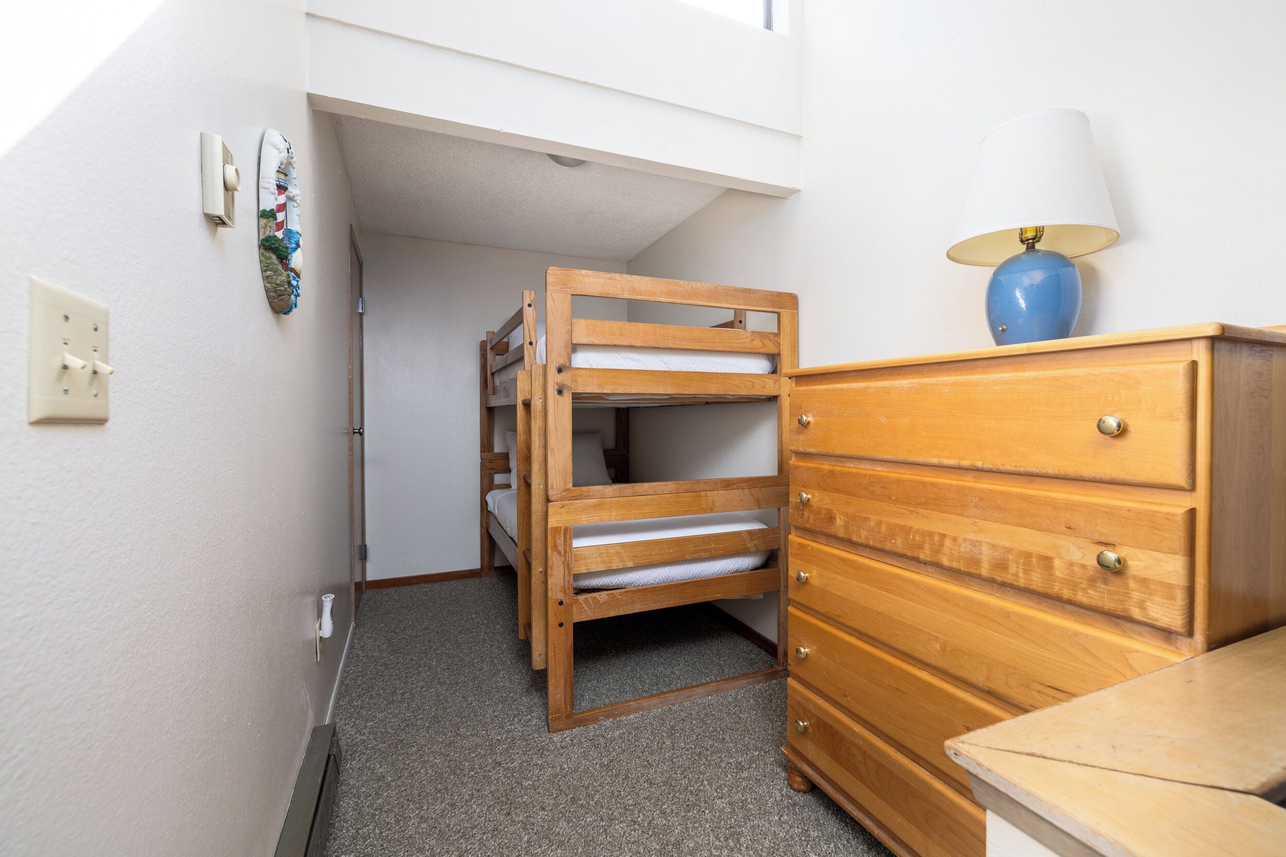 A bunk bed with a wooden frame, a wooden dresser with drawers, and a lamp on top.