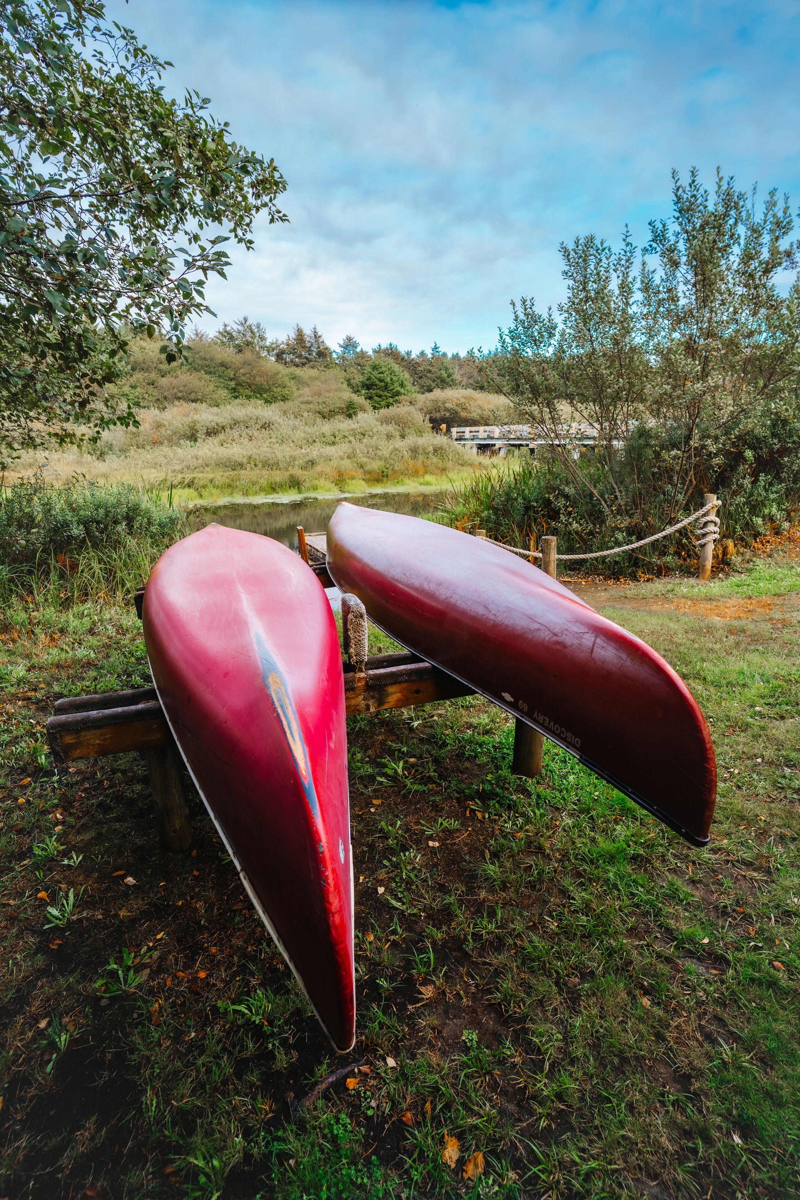 Two red paddle boats parked on a wooden dock in a natural setting with trees and a grassy area.