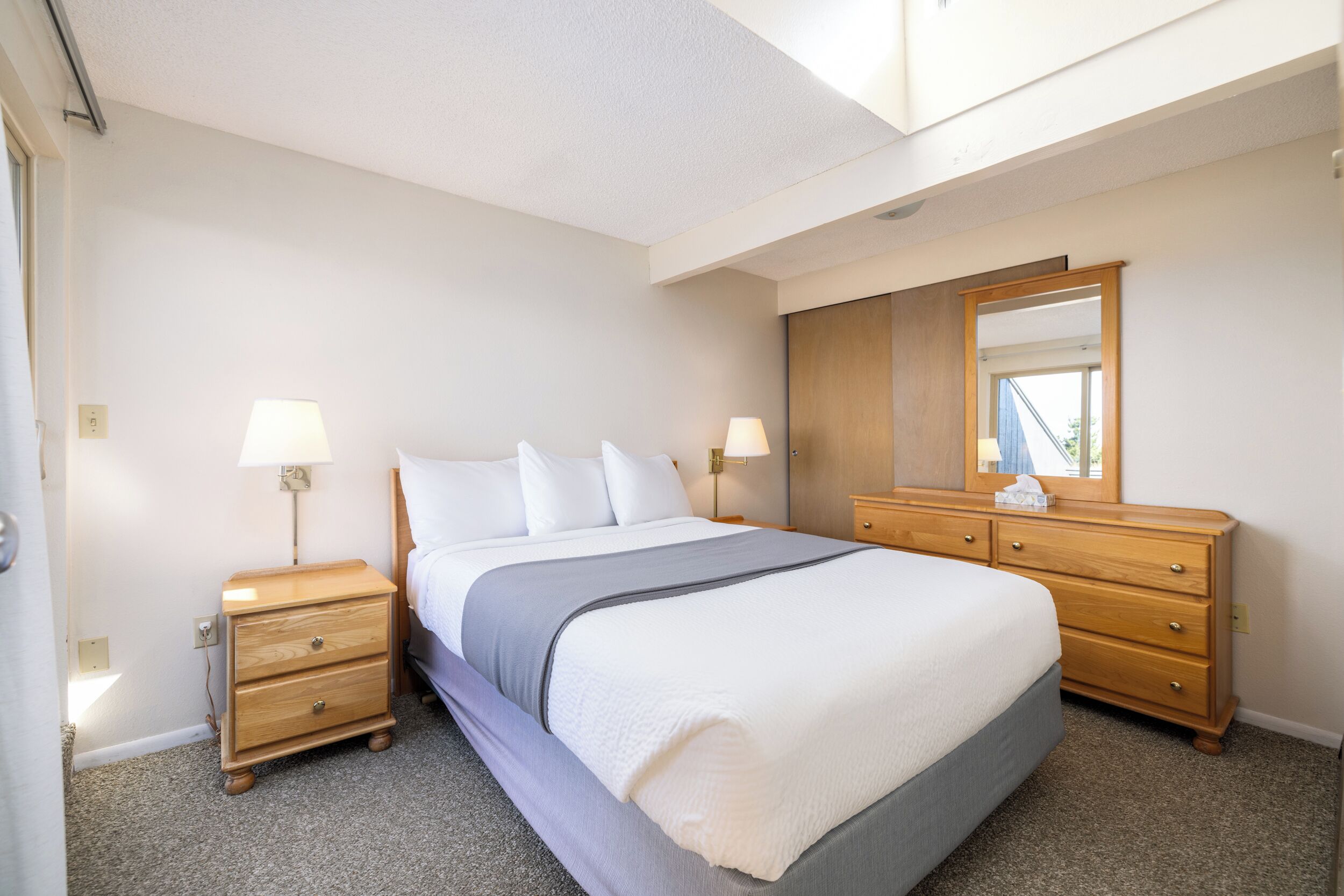 A neatly arranged bedroom with a large bed, bedside tables, a dresser, and a mirror.