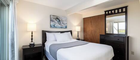 A neatly arranged bedroom with a large bed, two bedside tables with lamps, a dresser, and a mirror.