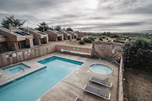 Un área de piscina con dos piscinas, sillas de descanso y una terraza de madera.