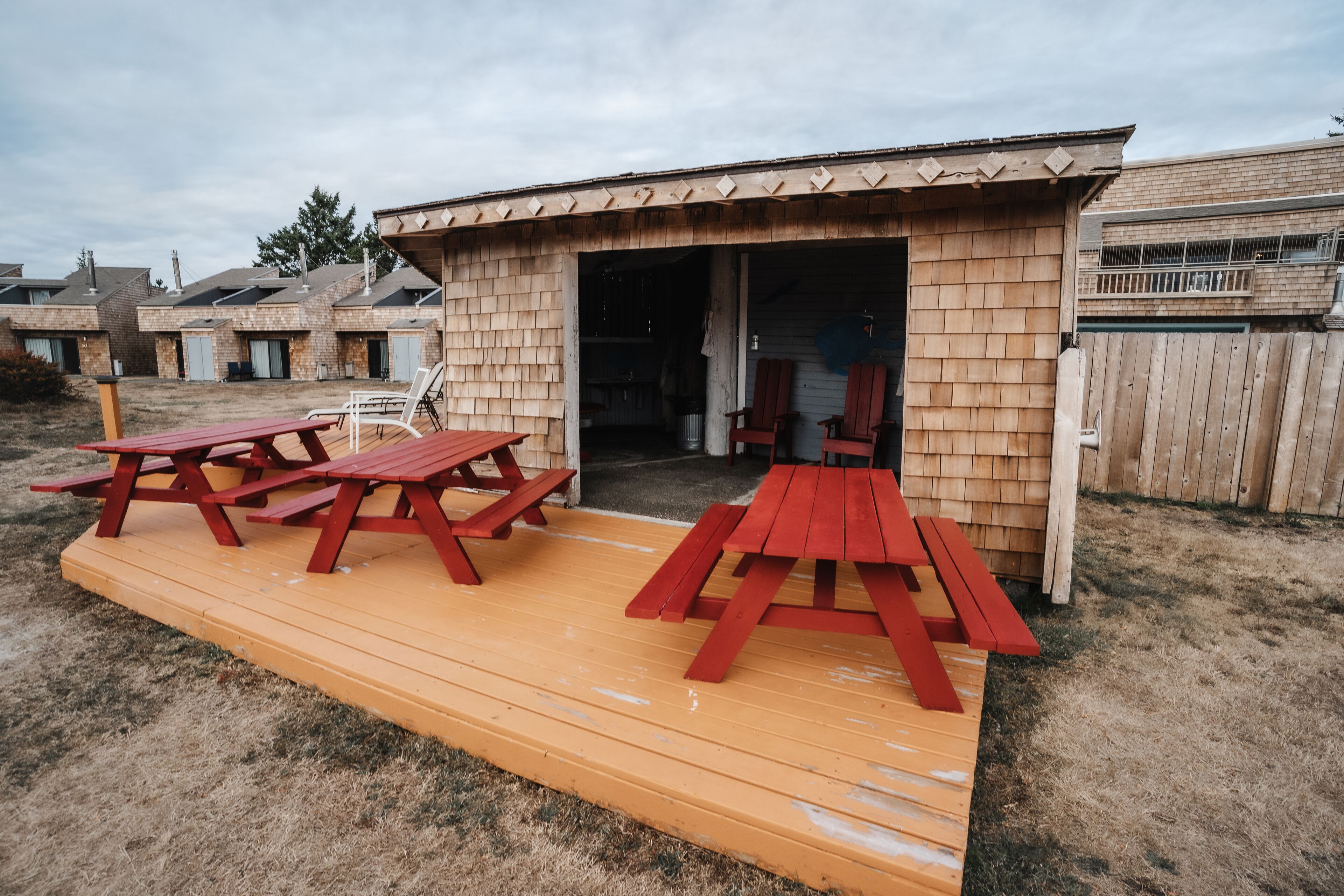 A wooden structure with a covered patio area, featuring picnic tables and a door leading to an interior space.