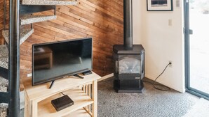 Un interior moderno con una escalera espiral, una estufa de leña y un televisor sobre un pedestal de madera.