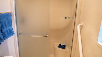 Een kleine, afgesloten douchecel met een glazen deur, een toilet en een handdoekhouder.