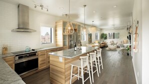 A modern kitchen with wooden cabinets, a large island with bar stools, stainless steel appliances, and pendant lighting.