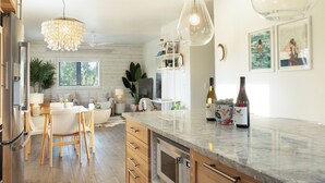 A modern kitchen with wooden cabinets, a marble countertop, and pendant lighting.