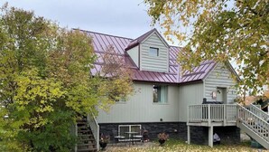 A two-story house with a metal roof, a covered porch, and a stone foundation. - The Farmhouse - Clean, comfortable, and affordable! (Fairbanks)