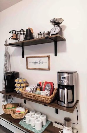 Een keukenhoek met planken waarop koffiezetapparatuur, een koffiemolen en een weegschaal staan.