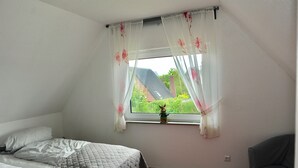Un dormitorio con una cama, una ventana con cortinas, una pequeña figura en el alféizar y una silla.