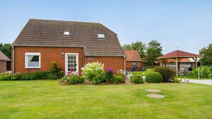 Ein Ziegelhaus mit einem Ziegeldach, ein kleiner Garten mit verschiedenen Pflanzen und eine überdachte Sitzgelegenheit im Freien.