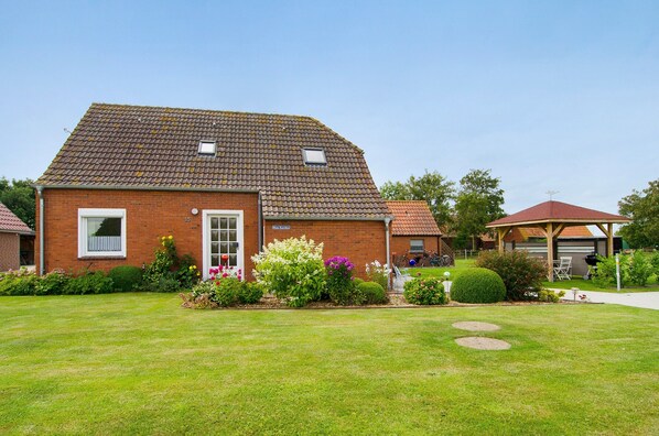 A brick house with a tiled roof, a small garden with various plants, and a covered outdoor seating area. - Holiday Home 'Huus Karoline' with Garden & Wi-Fi (Hagermarsch Junkersrott)