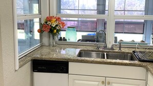 Une cuisine avec des meubles blancs, un plan de travail en granit, un lave-vaisselle et une fenêtre donnant sur l’extérieur.