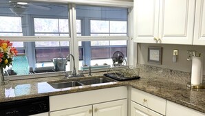 Une cuisine avec des meubles blancs, un plan de travail en granit, un lave-vaisselle, une fenêtre avec vue et un luminaire au plafond.