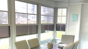 Un coin repas avec une table ronde et six chaises, de grandes fenêtres et un ventilateur de plafond.