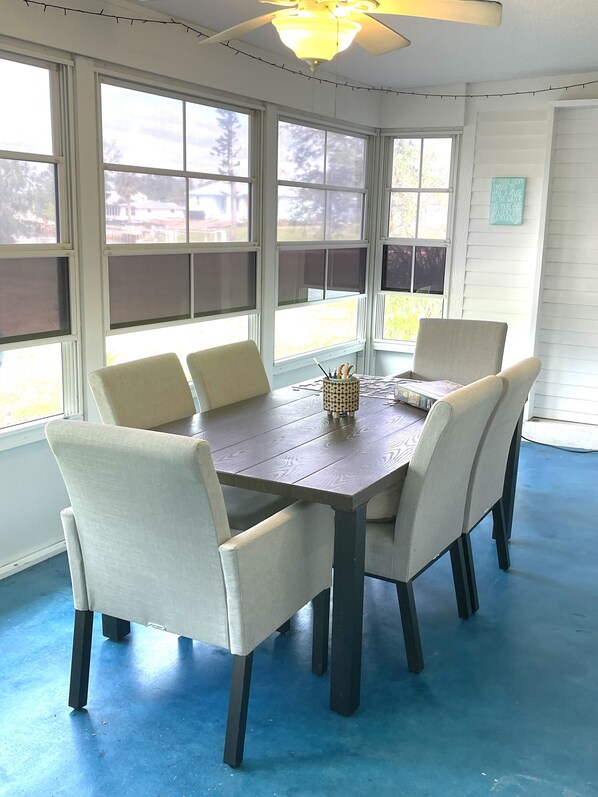 Un coin repas avec une table ronde et six chaises, de grandes fenêtres et un ventilateur de plafond.