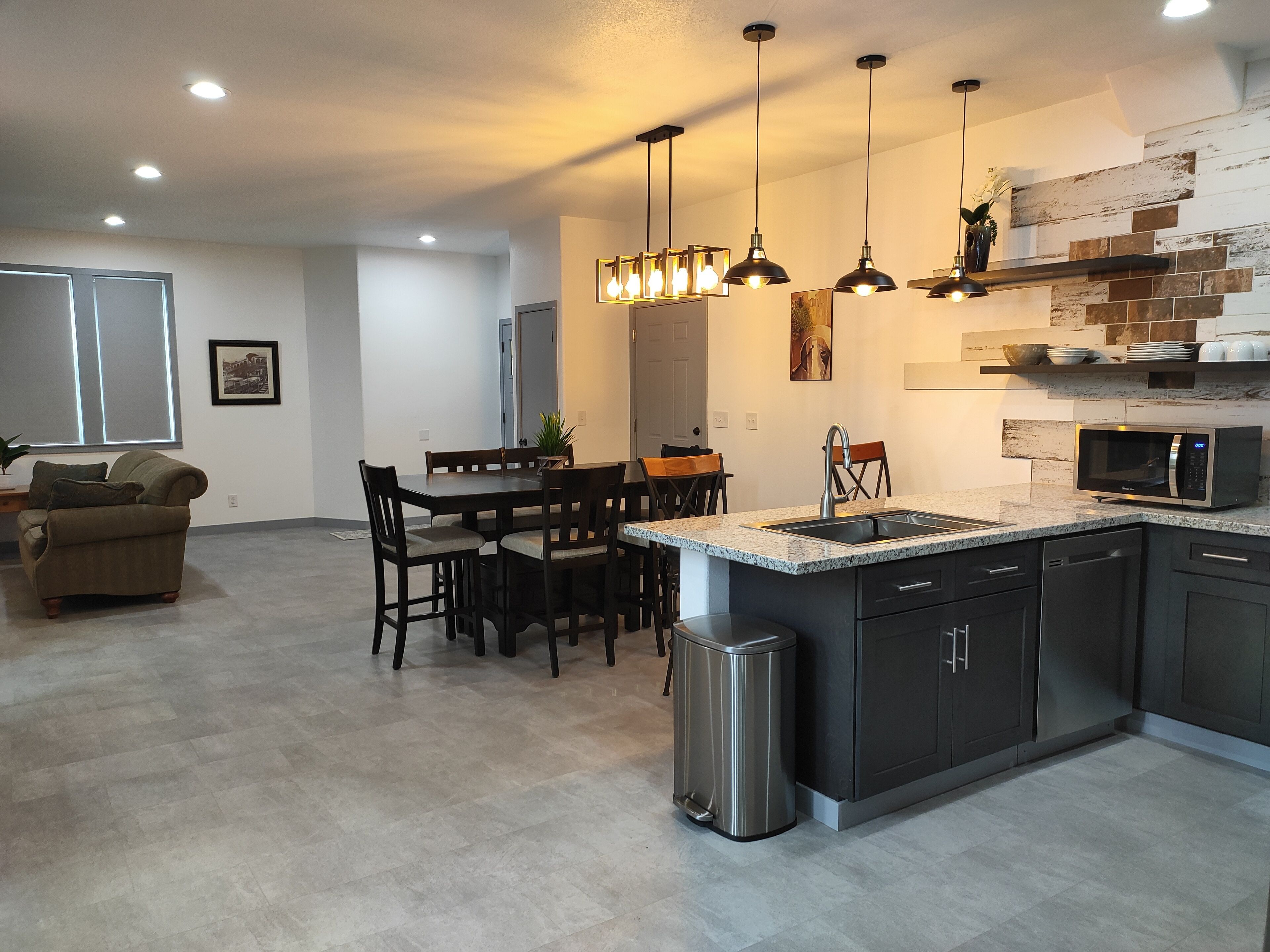 A modern kitchen with dark cabinetry, a granite countertop, a stainless steel sink, and a built-in microwave.