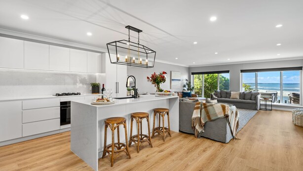 A modern kitchen with white cabinetry, a central island with stools, and a dining area with a view of the beach.