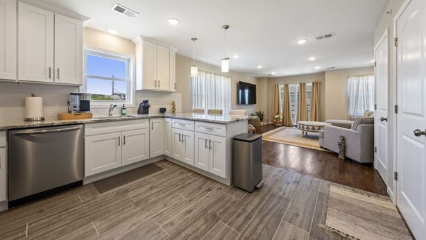 A modern kitchen with white cabinets, a stainless steel dishwasher, and a large island.