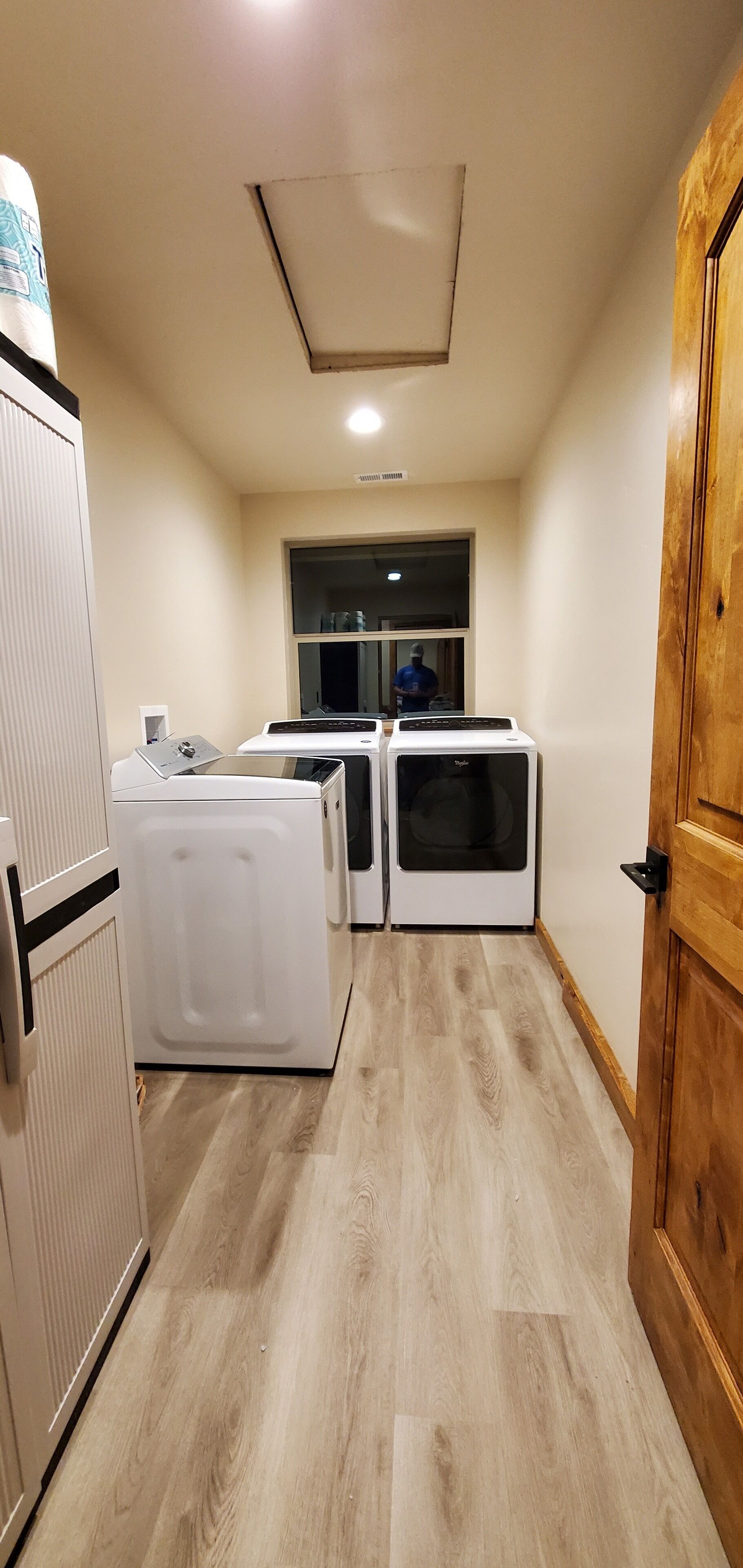 Une buanderie équipée de deux machines à laver et d’un sèche-linge, avec un plancher en bois et une porte située à droite.