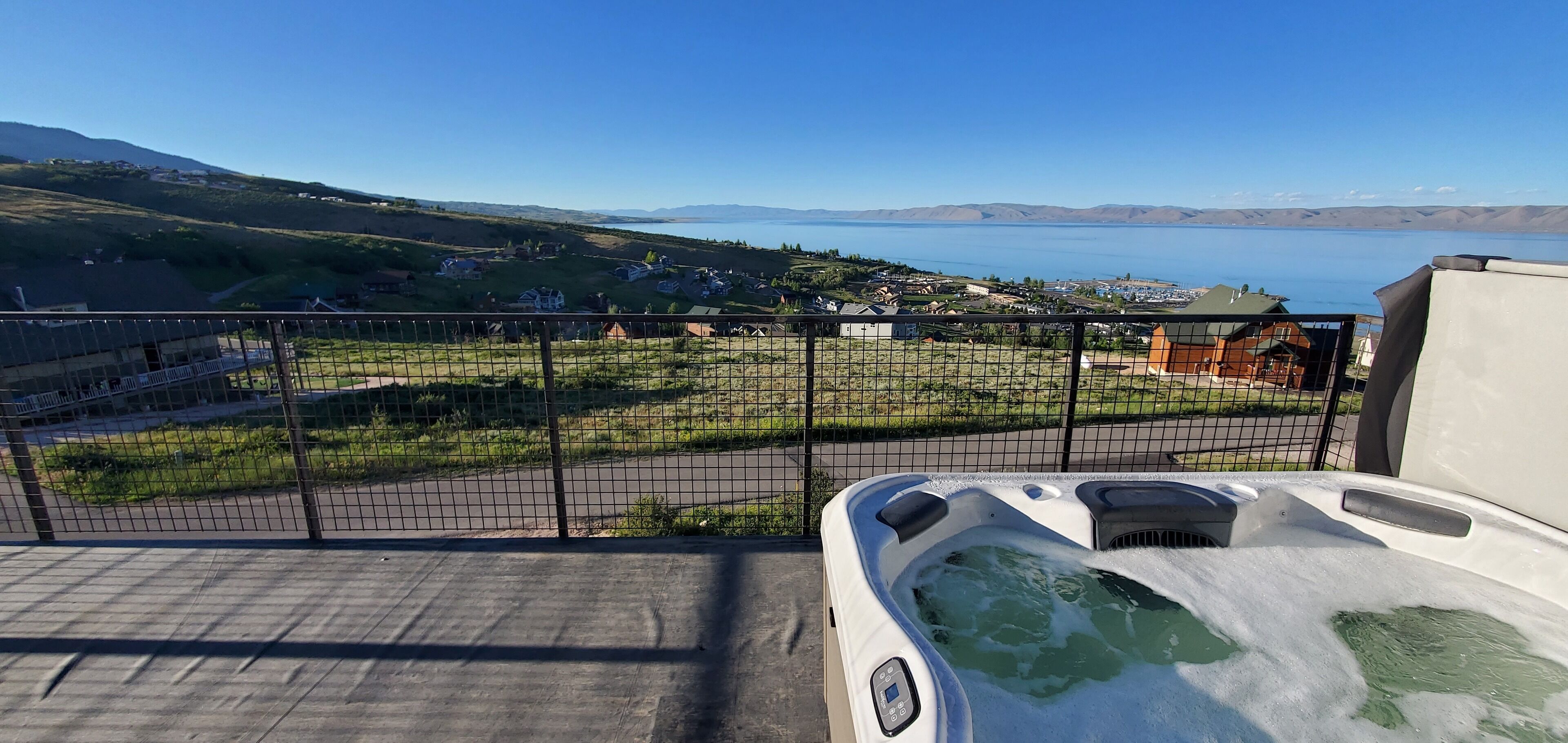 Un jacuzzi sur un balcon donnant sur un quartier résidentiel, avec un lac et des montagnes visibles au loin.