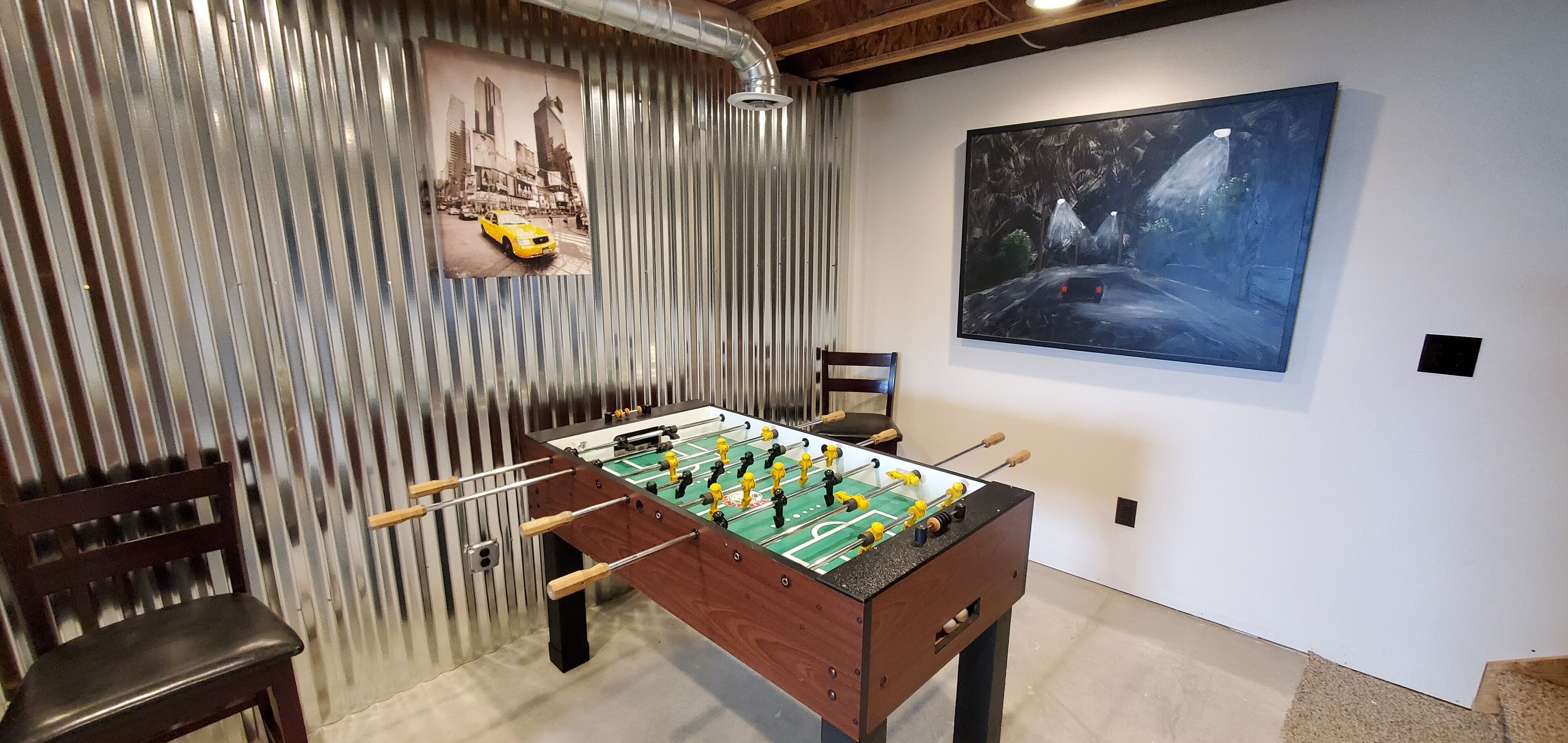 Una habitación con mesa de fútbol, una silla, un cuadro y una rejilla de ventilación.