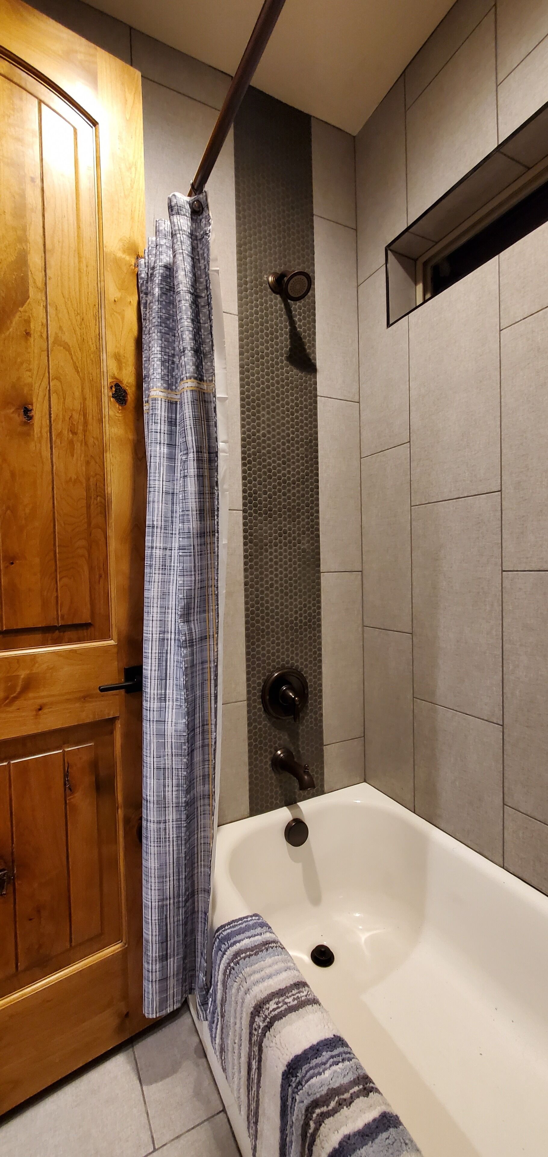 Un baño con puerta de madera, cortina de ducha, bañera y paredes con azulejos.