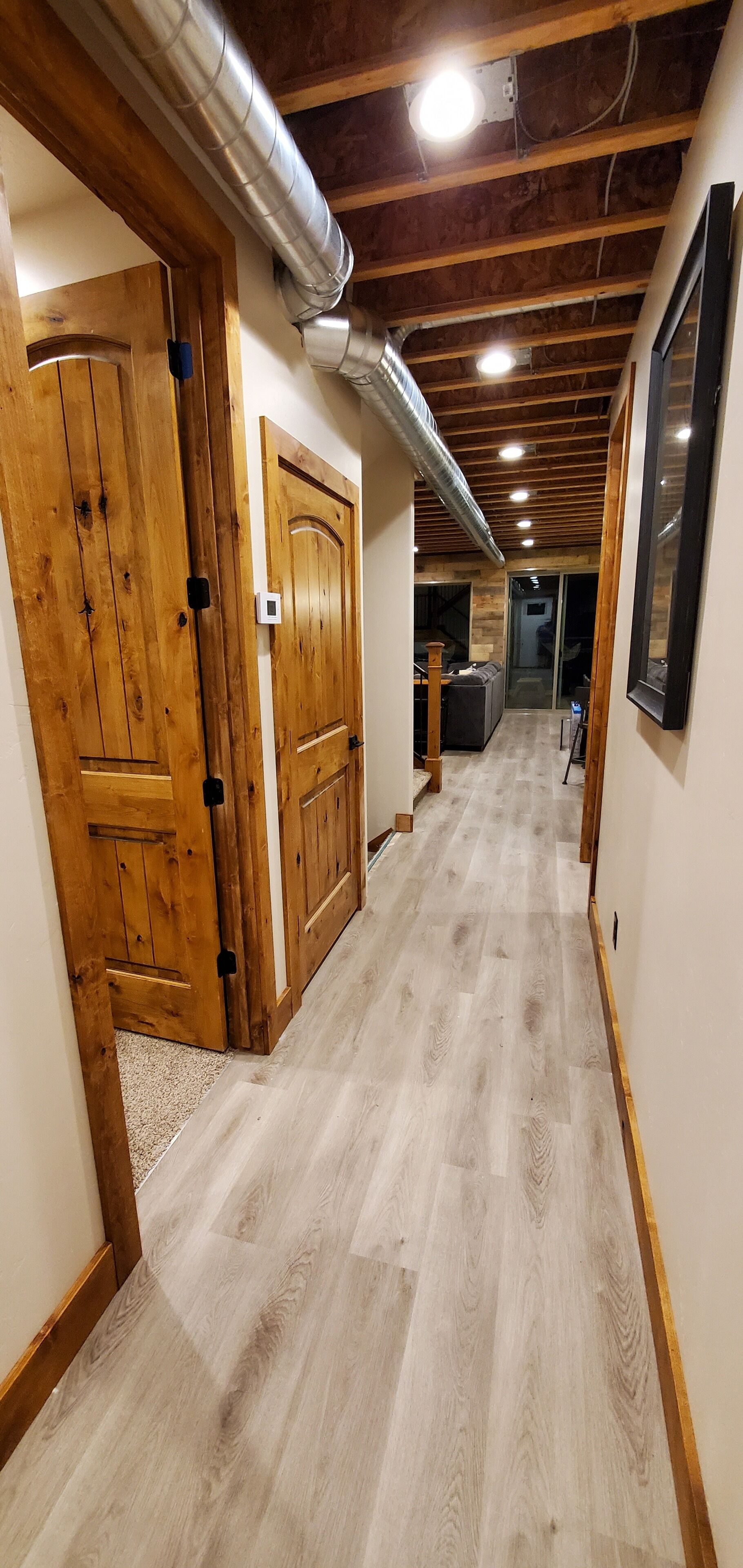 A hallway with wooden doors, a light-colored wooden floor, and a ceiling with exposed beams and ductwork.