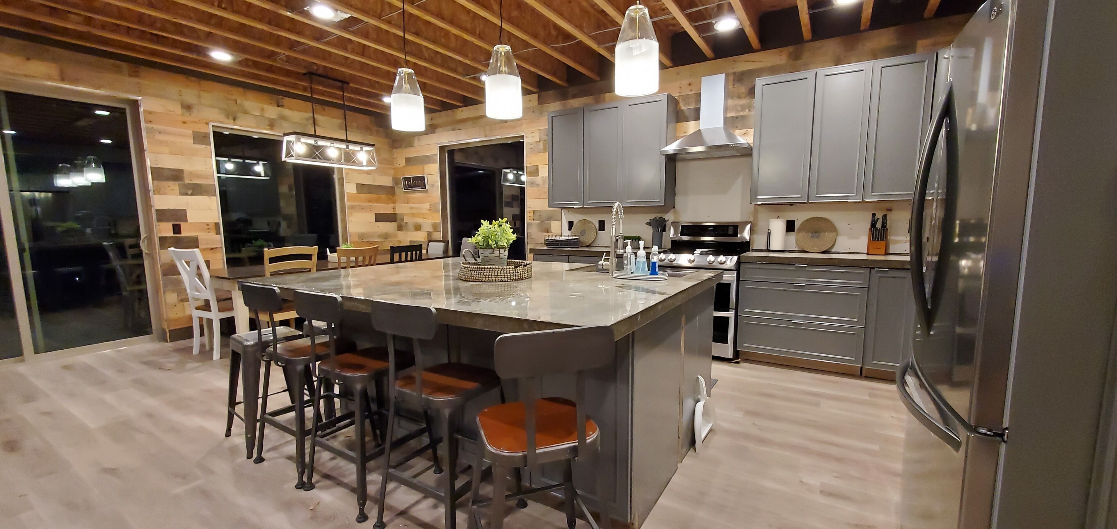 Une cuisine moderne dotée d’un îlot central, de tabourets de bar, d’appareils électroménagers en acier inoxydable et d’éléments décoratifs en bois.