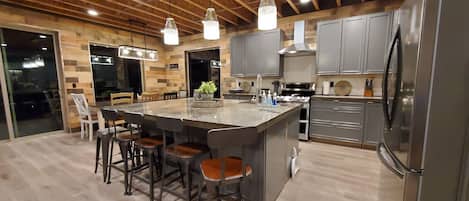 Une cuisine moderne dotée d’un îlot central, de tabourets de bar, d’appareils électroménagers en acier inoxydable et d’éléments décoratifs en bois.