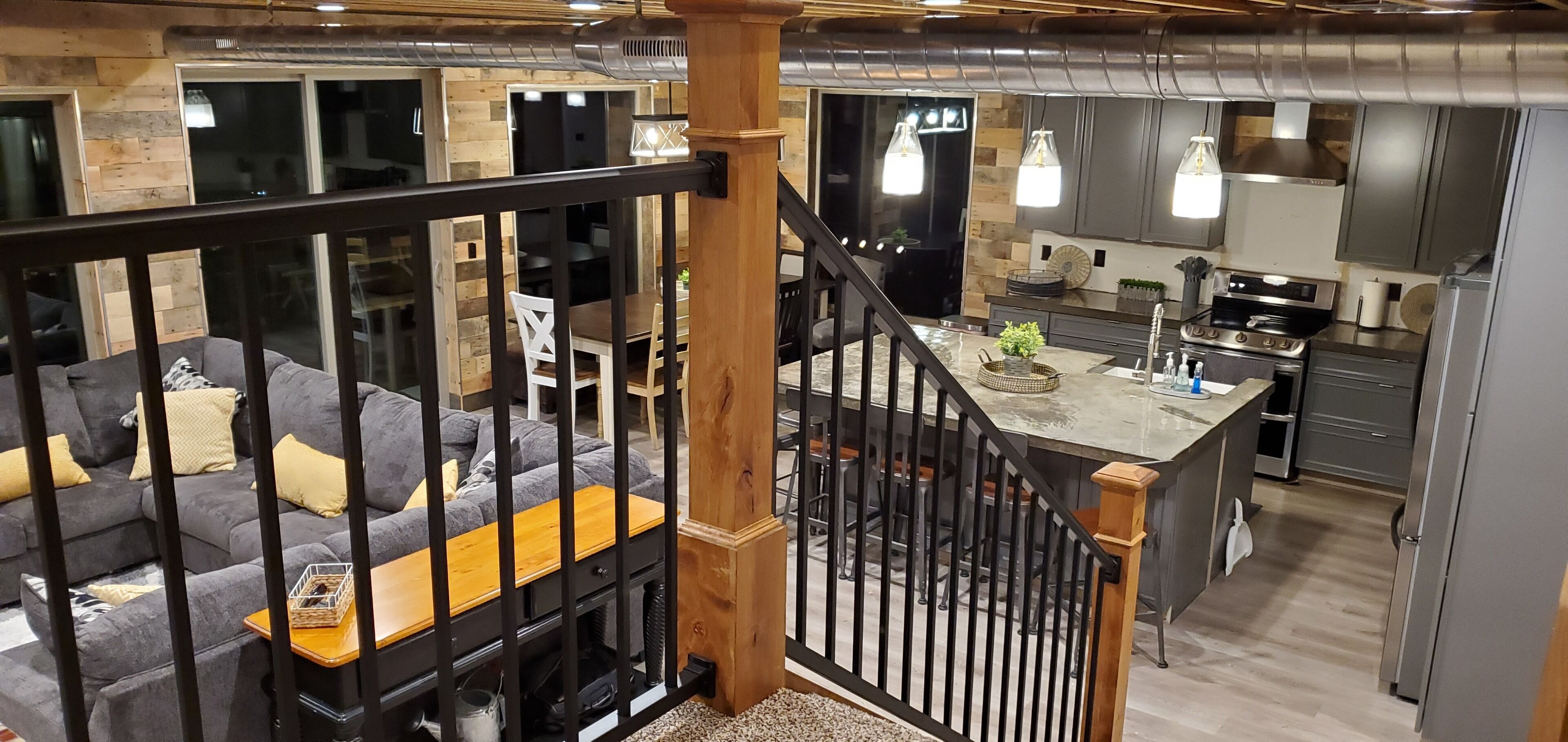A modern interior with a living area featuring a gray sofa and a wooden coffee table, a kitchen with stainless steel appliances, and a staircase with a wooden railing.