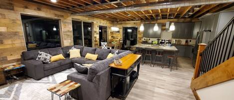 A modern living room with a sectional sofa, a wooden coffee table, and a kitchen area with bar stools.