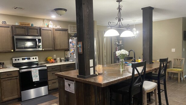 A kitchen with wooden cabinets, stainless steel appliances, a central island with bar stools, and a chandelier.