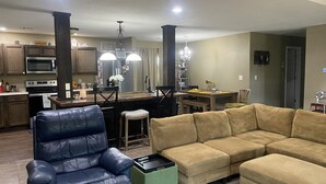 A modern living room with a leather sofa, a green ottoman, and a beige sectional.
