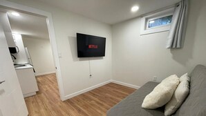 Quarto com um sofá cinzento, uma TV de tela plana na parede e piso de madeira.