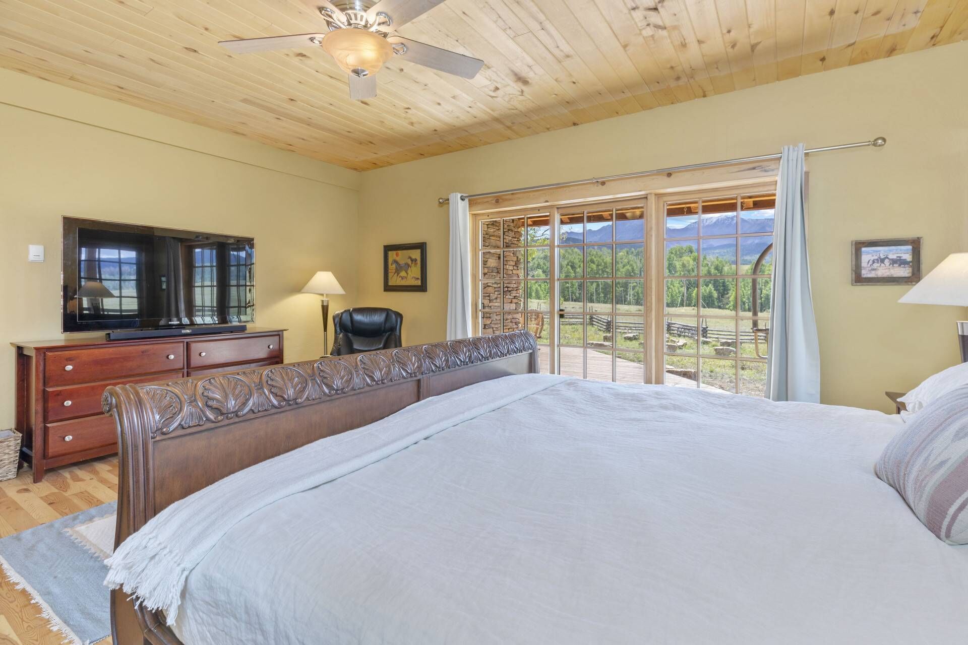 Un dormitorio con una cama grande, televisión, escritorio y silla. Se ve una ventana con vistas al exterior.