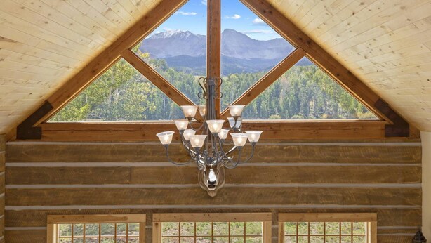 A log cabin interior with a large triangular window and a chandelier. - Posey Meadow Ranch - Wilson Mesa, 70 Acres with Views upon Views (Placerville)