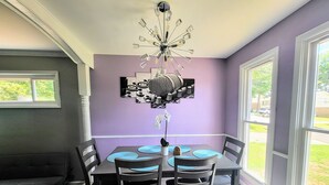 Un coin repas avec une table dressée pour quatre personnes, un lustre et une vue sur l’extérieur grâce à de grandes fenêtres.