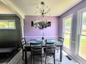 Un coin repas avec une table dressée pour quatre personnes, un lustre et une vue sur l’extérieur grâce à de grandes fenêtres.