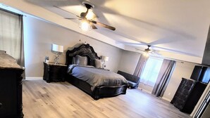 Une chambre avec un grand lit, un ventilateur de plafond et un plancher en bois.