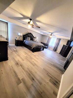 Une chambre avec un grand lit, un ventilateur de plafond et un plancher en bois.