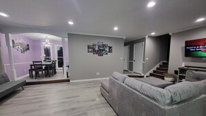Un salon moderne avec un canapé gris, un coin repas agrémenté d’un lustre et un escalier menant à un autre niveau.