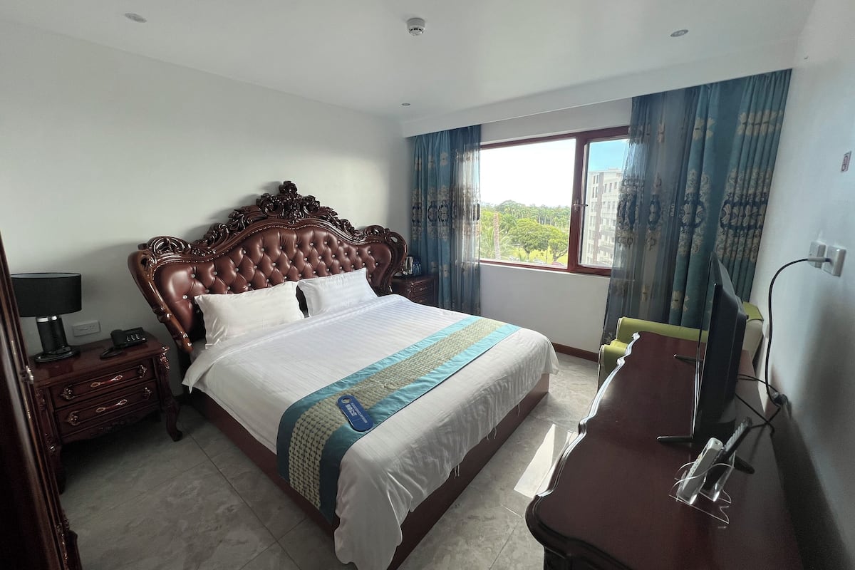 A hotel room with a large bed, a desk with a chair, a TV, and a window with curtains.