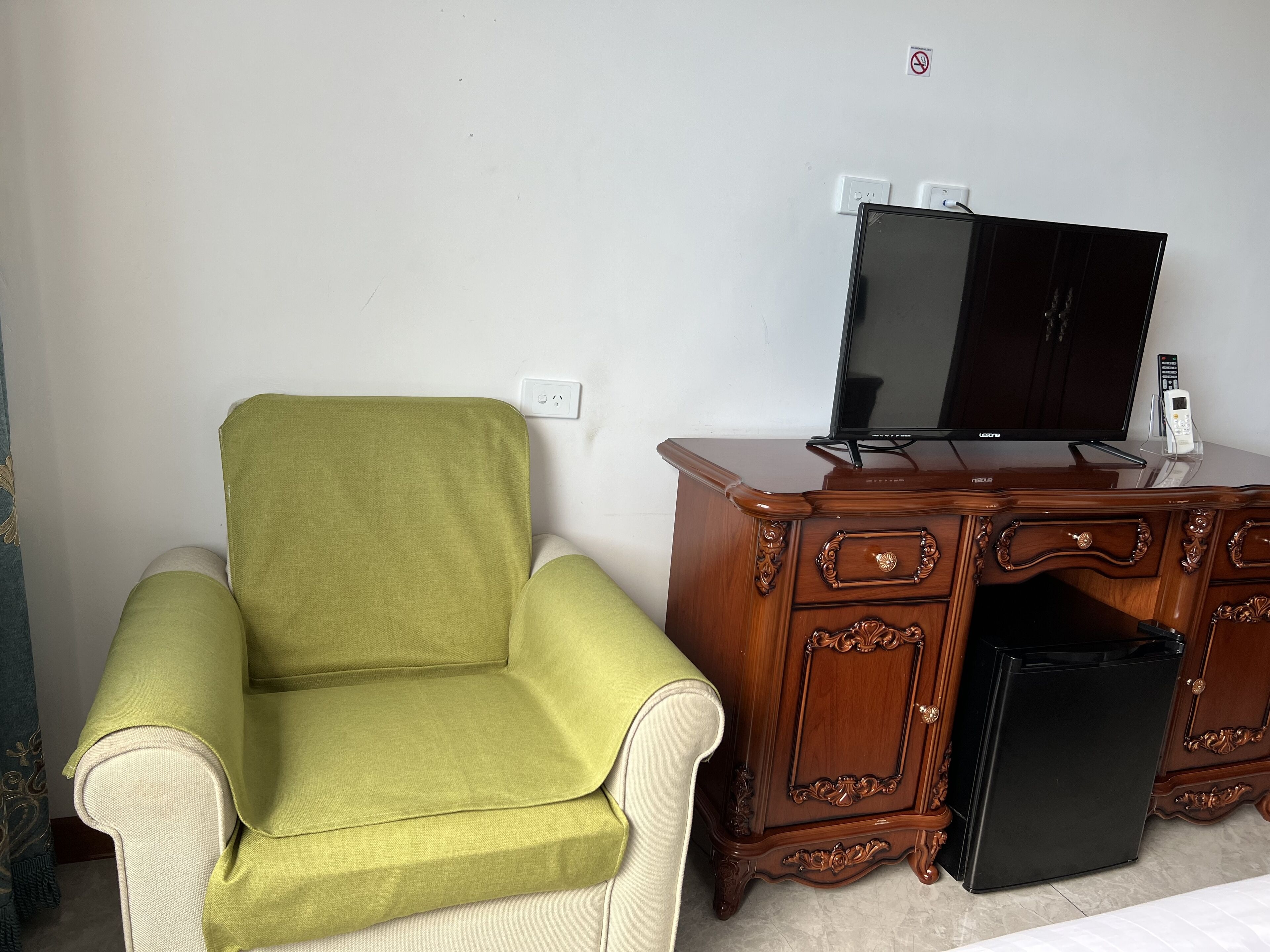 Una habitación con un sillón verde, un mueble de madera con televisor y un electrodoméstico pequeño y negro.
