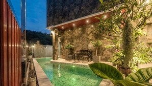 A swimming pool with a stone wall and plants, a wooden deck, and a patio area with outdoor furniture. - Exclusive Villa Stan with Top Amenities (Kamala)