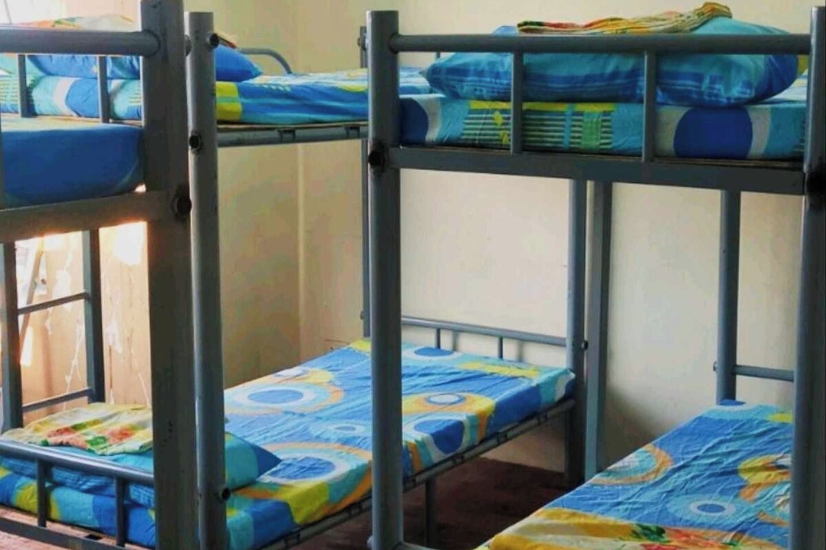 A dormitory with bunk beds, wooden flooring, and a window.