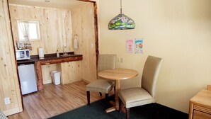Ett kompakt kök med träpanel på väggarna, ett litet kylskåp, en diskho och en matplats med ett runt bord och två stolar.