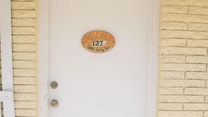 A white door with a welcome sign and a number plate indicating the address.